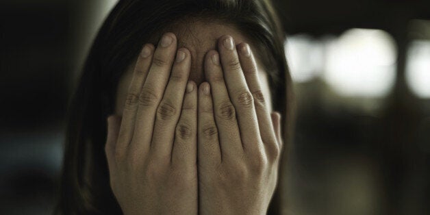 A young woman looking anxious and fearful with her hands over her eyes