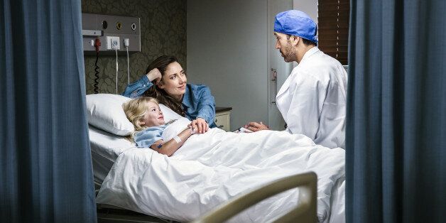 Little girl in a hospital bed with her mom by her side speaking to a doctor.