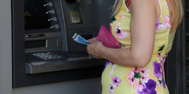 A woman uses an ATM of a bank after the government's decision last week to limit daily cash withdrawals to 60 euro ($66) in Athens, Tuesday, July 7, 2015. Greek Prime Minister Alexis Tsipras was heading Tuesday to Brussels for an emergency meeting of eurozone leaders, where he will try to use a resounding referendum victory to eke out concessions from European creditors over a bailout for the crisis-ridden country. (AP Photo/Petr David Josek)