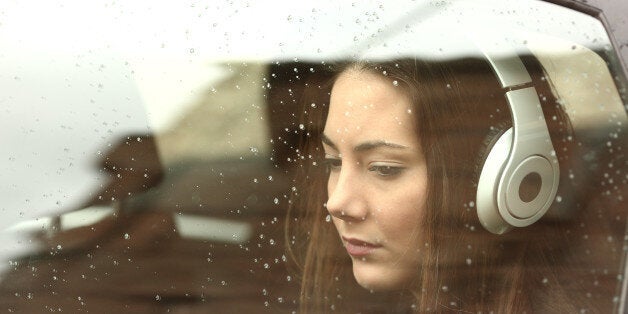 Sad teenager girl inside a car with headphones listening to the music