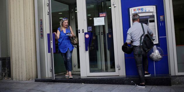 A customer enters a Eurobank Ergasias SA bank branch as a man uses an automated teller machine (ATM) outside shortly after opening in Athens, Greece, on Monday, July 20, 2015. German Chancellor Angela Merkel held out the prospect of limited debt relief as crisis-ravaged Greece prepares to reopen its banks three weeks after they were shut. Photographer: Matthew Lloyd/Bloomberg via Getty Images
