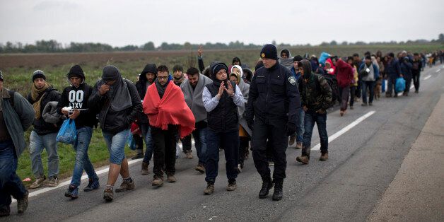 A woman talks with a Croatian police officer as a group of people walk towards a registration center for migrants and refugees in Opatovac, Croatia, Tuesday, Oct. 20, 2015. Croatia's interior minister says his country is trying to coordinate the transfer of migrants with Slovenia, which has accused its neighbor of failing to manage the relentless flow of people. (AP Photo/Marko Drobnjakovic)