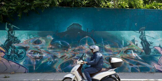 A rider drives his scooter past graffiti in Athens on Thursday, June 4, 2015. High-ranking members of Greece's governing radical left Syriza party say they cannot accept a deal proposed by the country's creditors during a meeting between Prime Minister Alexis Tsipras and the head of the European Union's executive arm. (AP Photo/Thanassis Stavrakis)