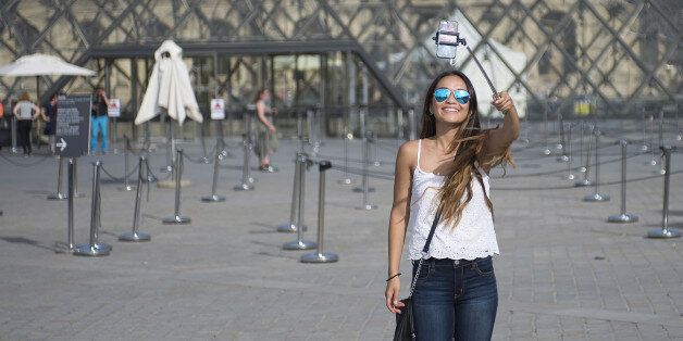 PARIS, FRANCE - AUGUST 06: A tourist takes a selfie using a selfie stick in front of the Louvre Pyramid on August 6, 2015 in Paris, France. Using a selfie stick has become a more and more common place among tourists but a number of high-profile attractions in Paris and other cities have started to ban them over fears of potential damage to exhibits. (Photo by Vanni Bassetti/Getty Images)