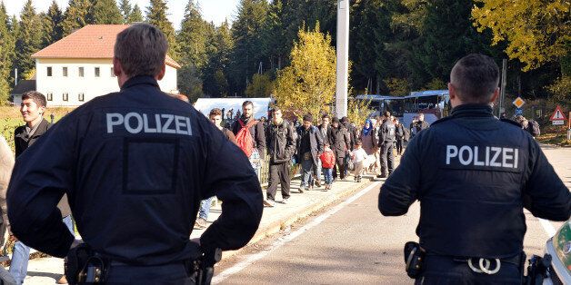 German police officers watch migrants crossing the border between Austria and Germany in Wegscheid near Passau, Germany, Wednesday, Oct. 28, 2015. Germany has implemented a plan to streamline the asylum process for those fleeing civil war, such as Syrians, to settle them more quickly, but also to more rapidly send home those whose case for asylum is weak. (AP Photo/Kerstin Joensson)