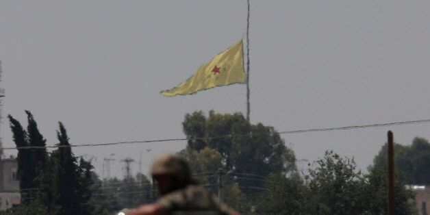 In this photo taken from the Turkish side of the border between Turkey and Syria, in Turkish soldier on an armoured personnel carrier in Akcakale, southeastern Turkey, watches as in the background a flag of the Kurdish People's Protection Units, or YPG, is raised over the city of Tal Abyad, Syria, Tuesday, June 16, 2015. Kurdish fighters with the YPG, captured large parts of the strategic border town of Tal Abyad from the Islamic State group Monday, dealing a huge blow to the group which lost a key supply line for its nearby de facto capital of Raqqa, a spokesman for the main Kurdish fighting force said. (AP Photo/Lefteris Pitarakis)