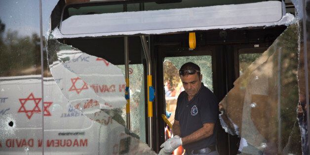 An Israeli police officer inspects the scene of a shooting attack in Jerusalem, Tuesday, Oct. 13, 2015. A pair of Palestinian men boarded a bus in Jerusalem and began shooting and stabbing passengers, while another assailant rammed a car into a bus station before stabbing bystanders, in near-simultaneous attacks that escalated a monthlong wave of violence. Two Israelis and one attacker were killed. (AP Photo/Oded Balilty)