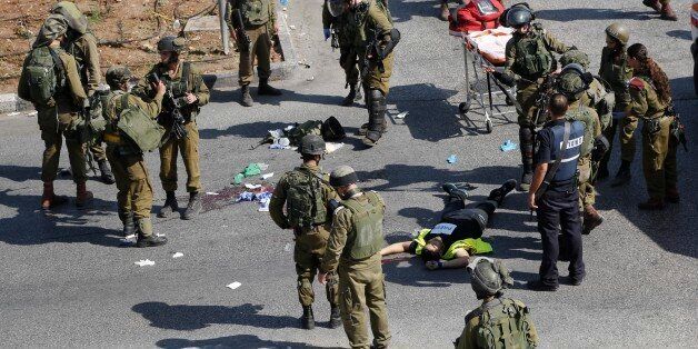 Israeli soldiers stand around the body of a Palestinian, seen on the ground, who was shot and killed after stabbing an Israeli soldier during clashes in Hebron, West Bank Friday, Oct. 16, 2015. The Palestinian man wearing a yellow