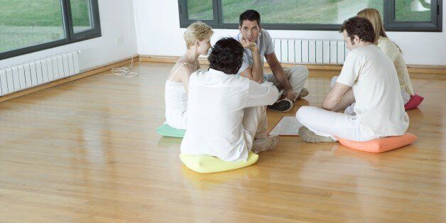 Group therapy session, adults sitting in circle on floor, talking