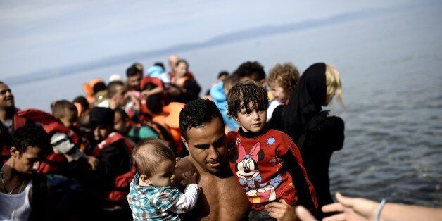 A man carries two children as refugees and migrants arrive on an inflatable dinghy to the Greek island of Lesbos after crossing the Aegean sea from Turkey on September 26, 2015. UN Secretary-General Ban Ki-moon welcomed the European Union's decision to inject $1 billion to help countries overwhelmed by Syrian refugees, but said more must be done to relocate migrants. AFP PHOTO / ARIS MESSINIS (Photo credit should read ARIS MESSINIS/AFP/Getty Images)