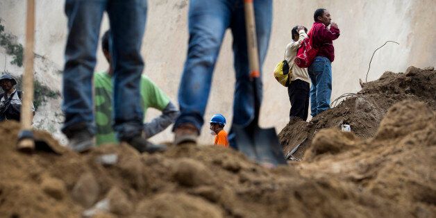 Neighbors, right, look on as they wait for news as rescue workers continue the search at the site of a landslide in Cambray, a neighborhood in the suburb of Santa Catarina Pinula, about 10 miles east of Guatemala City, Saturday, Oct. 3, 2015. The hill that towers over Cambray collapsed late Thursday after heavy rains, burying several houses with dirt, mud and rocks. The death toll rose to 30 amid fears that hundreds more could still be buried in the rubble. (AP Photo/Moises Castillo)