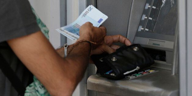 A man uses an ATM of a bank after the government's decision last week to limit daily cash withdrawals to 60 euro ($66) in Athens, Tuesday, July 7, 2015. Greek Prime Minister Alexis Tsipras was heading Tuesday to Brussels for an emergency meeting of eurozone leaders, where he will try to use a resounding referendum victory to eke out concessions from European creditors over a bailout for the crisis-ridden country. (AP Photo/Petr David Josek)