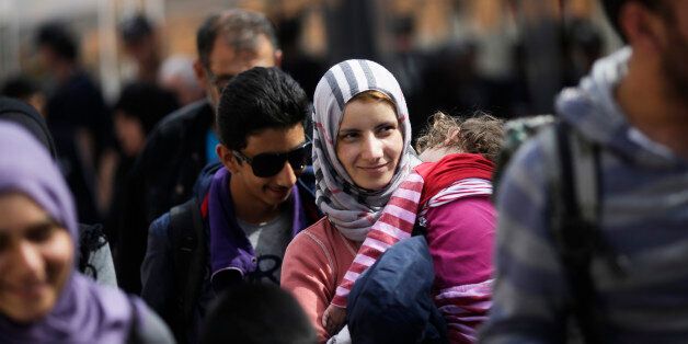 A woman with a baby, saying they are from Syria, arrives with other refugees at the train station of the southern German border town Passau, Tuesday, Sept. 15, 2015, after they have been taken off a train by German border police for registration. Germany introduced temporary border controls Sunday to stem the tide of thousands of refugees streaming across its frontier, sending a clear message to its European partners that it needs more help with an influx that is straining its ability to cope. (AP Photo/Markus Schreiber)