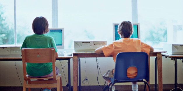 Rear view of two boys sitting in front of computers