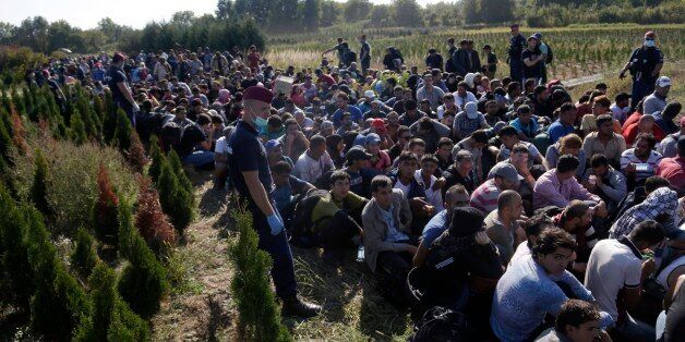 A group of migrants sits and waits to be escorted to a train after crossing a border from Croatia near the village of Zakany, Hungary, Wednesday, Sept. 23, 2015. Deeply divided European Union leaders have been called to an emergency summit to seek long-term responses to the continent's ballooning crisis of refugees and migrants, a historic challenge EU President Donald Tusk said the bloc has failed dismally to meet. (AP Photo/Petr David Josek)