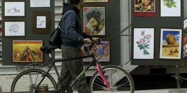 A man wheels his cycle past an exhibition of artwork by convicted November 17 left-wing terrorists, hosted in the grounds of the National Technical University in Athens, Greece, on Tuesday Nov. 15, 2005. The building is the focus of celebrations, starting Tuesday, for the 32nd anniversary of a student uprising that helped bring down the military dictatorship that ruled Greece from 1967-74. Fifteen members of the left-wing group, named after the 1973 uprising, were jailed in 2003 for terrorist activities. The group killed 23 people in a string of attacks between 1975 and 2000. (AP Photo/Petros Giannakouris)