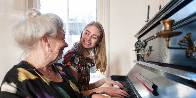 Grandmother and granddaughter sitting next to each other and playing the piano.