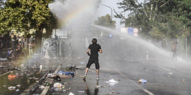 A man stands opposite Hungarian riot police using water cannon to push back refugees at the Hungarian border with Serbia near the town of Horgos on September 16, 2015. Europe's 20-year passport-free Schengen zone appeared to be a risk of crumbling with Germany boosting border controls on parts of its frontier with France as migrants desperate to find a way around Hungary's border fence began crossing into Croatia. With a string of EU countries tightened frontier controls in the face of the unpre