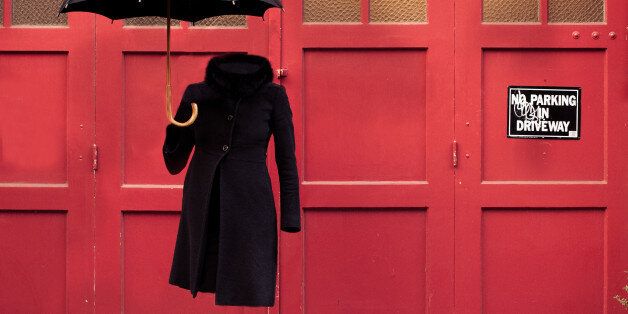 'Invisible' woman in winter coat with high heels and umbrella against red garage door.