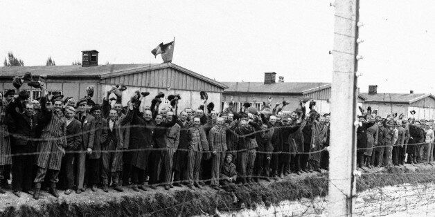 Prisoners at the electric fence of Dachau concentration camp cheer the Americans in Dachau, Germany in an undated photo. Some of them wear the striped blue and white prison garb. They decorated their huts with flags of all nations which they had made secretly as they heard the guns of the 42nd Rainbow Div., getting louder and louder on the approach to Dachau. (AP Photo)