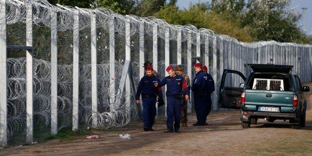 Hungarian police officers check a hole at the fence where migrants tried to cross the border line between Serbia and Hungary in Roszke, southern Hungary, Tuesday, Sept. 15, 2015. Hungary is set to introduce much harsher border controls at midnight â laws that would send smugglers to prison and deport migrants who cut under Hungary's new razor-wire border fence. The country's leader was emphatically clear that they were designed to keep the migrants out. (AP Photo/Matthias Schrader)