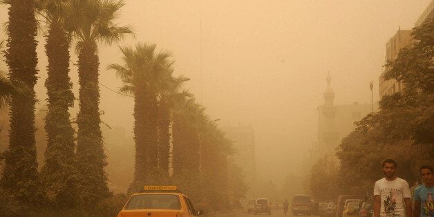 In this photo released by the Syrian official news agency SANA, Syrian citizens cross a street, as a sandstorm shrouds Damascus, Syria, Tuesday, Sept. 8, 2015. The unseasonal sandstorm hit Lebanon and Syria, reducing visibility and sending dozens to hospitals with breathing difficulties because of the fine dust. (SANA via AP)
