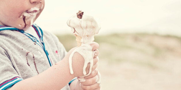 Little boy (3yrs) making a mess eating melting ice cream cone on beach.