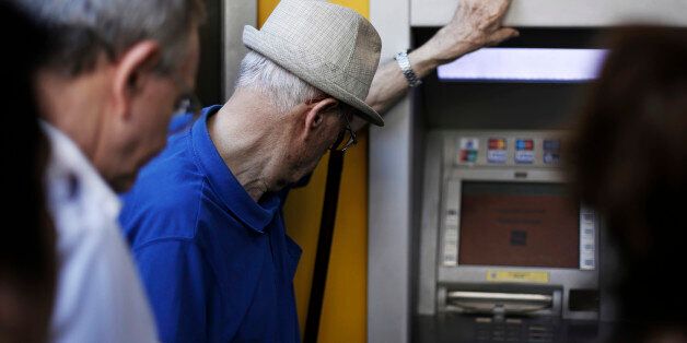 Pensioners and customers wait to withdraw cash from an automated teller machine (ATM) outside a Piraeus Bank SA bank branch in Thessaloniki, Greece, on Monday, July 6, 2015. European stocks dropped and the euro weakened as Greek voters' rejection of austerity sent investors to the relative safety of Treasuries, German bunds and the yen. Photographer: Konstantinos Tsakalidis/Bloomberg via Getty Images