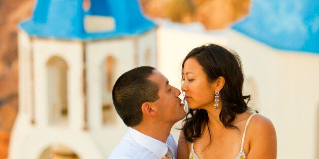 Asian couple kissing in from of churches in the town of Oia, Santorini