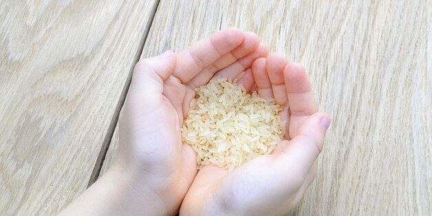 hand of the boy raised a handful of rice on wood texture