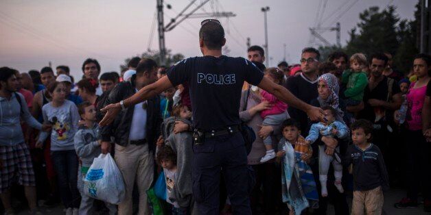 A Greek police officer gives orders to Syrian refugees as they wait to cross the border from Greece to Macedonia, in the border town of Idomeni , northern Greece, on Wednesday, Aug. 26, 2015. The U.N.âs refugee agency said it expects 3,000 people to cross Macedonia daily in the coming days. Greece has borne the brunt of a record number of refugees and migrants heading to Europe. (AP Photo/Santi Palacios)