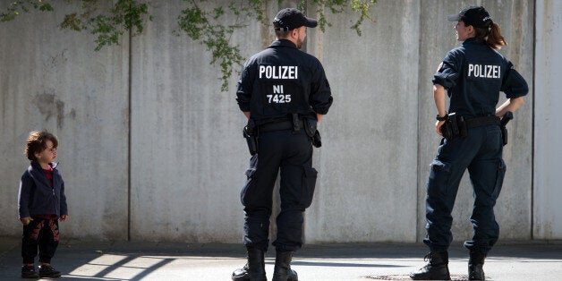 A child watches police prior to the visit of German Chancellor Angela Merkel to a refugee shelter that was attacked by far-right protesters over the weekend in Heidenau, near Dresden, eastern Germany, Wednesday, Aug. 26, 2015. ( Arno Burgi/dpa via AP)