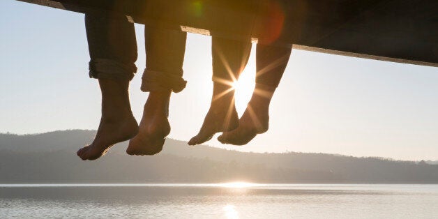 Couple's feet dangle from dock,above tranquil lake