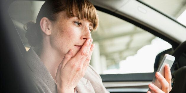 Portrait of businesswoman sitting in a car looking at her smartphone with hand on her mouth