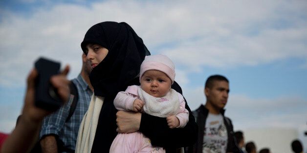 A Syrian refugee holds a baby after they arrived from eastern islands with a ferry at Athens' port of Piraeus, on Sunday, Aug. 23, 2015. Greece has been overwhelmed this year by record numbers of migrants. (AP Photo/Petros Giannakouris)