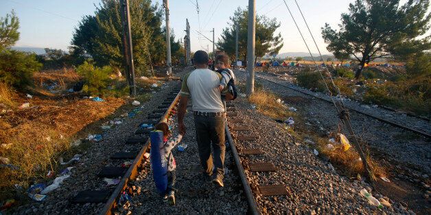 A migrant man carrying an infant in his arm takes a hand of another child as they walk on the train tracks near the train station of Idomeni, northern Greece, Sunday, Aug. 23, 2015. Macedonian police let small groups of migrants cross the border as many still continue to arrive from Greece at the border with Macedonia. (AP Photo/Darko Vojinovic)