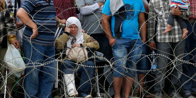 Migrants stand behind the barbed wire set by Macedonian police to stop thousands of migrants entering Macedonia illegally from Greece near the southern Macedonian town of Gevgelija, Saturday, Aug. 22, 2015. About 39,000 people, mostly Syrian migrants, have been registered as passing through Macedonia in the past month, twice as many as the month before. (AP Photo/Darko Vojinovic)