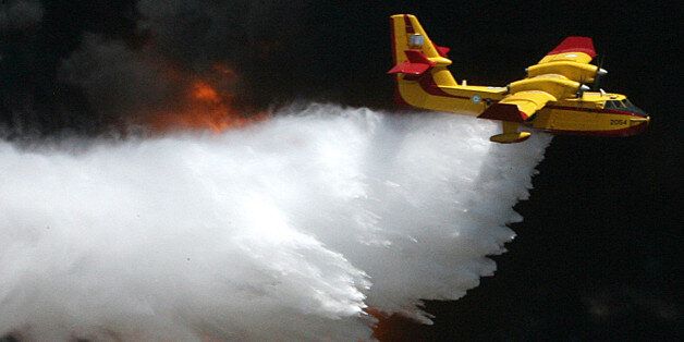 ** FILE ** A Greek Airforces Canadair CL-415 firefighting plane dumps water on flames at a solvent factory at the port of Lavrio, southeast of Athens, in this Wednesday, July 26, 2006 file photo. A similar type of plane crashed while battling a forest fire on the Greek island of Evia on Monday, July 23, 2007. Both crew members were killed when the plane slammed into a hillside amid thick clouds of smoke. Five firefighters and two civilians have died in fires in Greece this summer. (AP Photo/Kostas Tsironis)