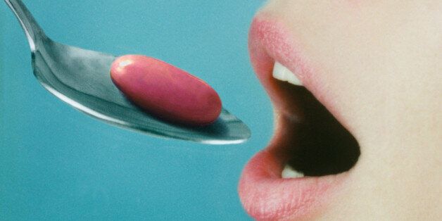 Woman opening mouth for spoon with pink pill on it, close-up