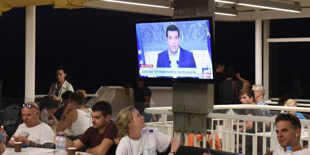 Greek Prime Minister Alexis Tsipras, on a screen during a televised address to the nation, as a tourist watches on a ferry traveling in the Aegean sea, near Syros island, Greece, Thursday, Aug. 20, 2015. Tsipras announced his governmentâs resignation and called early elections Thursday, seeking to consolidate his mandate to implement a new three-year international bailout that sparked a rebellion within his radical left Syriza party. (AP Photo/Giannis Papanikos)