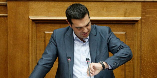 Greek Prime Minister Alexis Tsipras looks at his watch as he speaks to a parliamentary session in Athens, Friday, Aug. 14, 2015. Greek lawmakers approved their countryâs draft third bailout in a parliamentary vote Friday that relied on opposition party support and saw the government coalition suffer significant dissent.Â (AP Photo/Yannis Liakos)