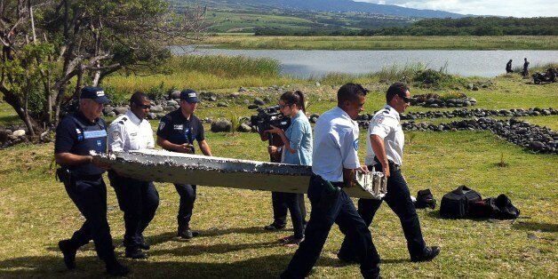 Police carry a piece of debris from an unidentified aircraft found in the coastal area of Saint-Andre de la Reunion, in the east of the French Indian Ocean island of La Reunion, on July 29, 2015. The two-metre-long debris, which appears to be a piece of a wing, was found by employees of an association cleaning the area and handed over to the air transport brigade of the French gendarmerie (BGTA), who have opened an investigation. An air safety expert did not exclude it could be a part of the Ma