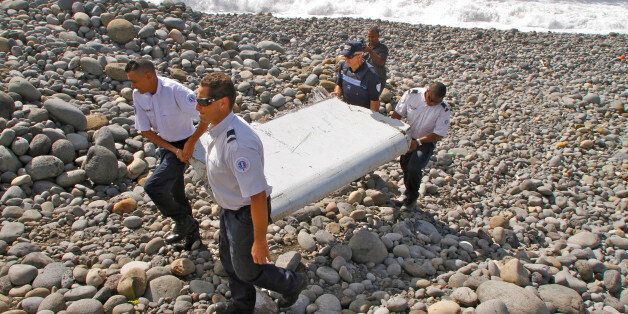In this photo dated Wednesday, July 29, 2015, French police officers carry a piece of debris from a plane in Saint-Andre, Reunion Island. Air safety investigators, one of them a Boeing investigator, have identified the component as a "flaperon" from the trailing edge of a Boeing 777 wing, a U.S. official said. Flight 370, which disappeared March 8, 2014, with 239 people on board, is the only 777 known to be missing. (AP Photo/Lucas Marie)