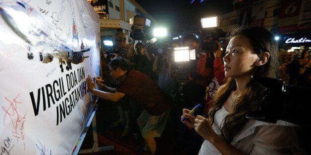 Kelly Wen, wife of Chinese passenger onboard the missing Malaysia Airlines Flight MH370 looks at a MAS airplane poster during an event to mark one year anniversary of the pane disappearance, during a candlelight vigil for passengers onboard the missing Malaysia Airlines Flight MH370 in Kuala Lumpur, Malaysia, on Friday, March 6, 2015. (AP Photo/Vincent Thian)