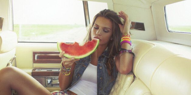 Beautiful young hipster woman eating piece of juicy watermelon on the back seat of the car. Shallow DOF; Soft focused; developed from RAW; retouched with special care and attention; small amount of grain added for best final impression; ready made for print and web use;