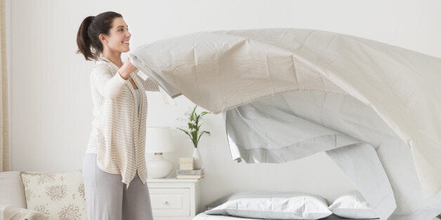 USA, New Jersey, Jersey City, Woman spreading sheet on bed