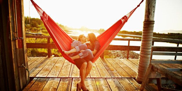 Husband and wife couple kissing in hammock on dock at sunset