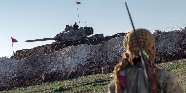 A Syrian Kurdish militia member of YPG patrols near a Turkish army tank as Turks work to build a new Ottoman tomb in the background in Esme village in Aleppo province, Syria, Sunday, Feb. 22, 2015. Turkey launched an overnight military operation into neighboring Syria to evacuate troops guarding an Ottoman tomb and to move the crypt to a new location, Turkish Prime Minister Ahmet Davutoglu said Sunday. Davutoglu said they plan to build a new Ottoman tomb in Esme village, close to Turkey-Syria border. (AP Photo/Mursel Coban, Depo Photos)