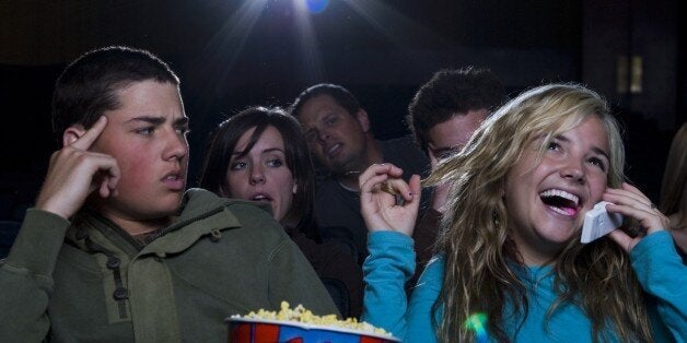 Girl talking on cell phone at movie theater with annoyed boy