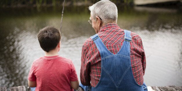 Color image of a young boy fishing with his grandfather while sitting on a dock.